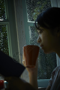 下雨天站在窗户前发呆的孤独女性图片