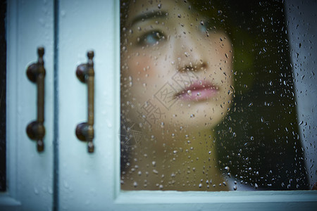 下雨天站在窗户前发呆的孤独女性家高清图片素材