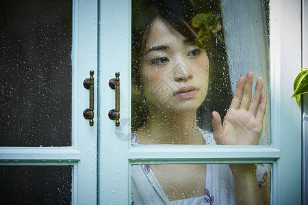 下雨天靠在窗边发呆的孤独女性青年高清图片素材