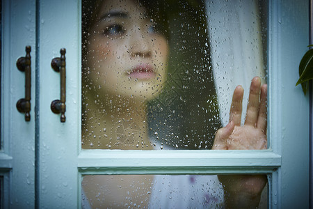 下雨天靠在窗边发呆的孤独女性面部表情高清图片素材