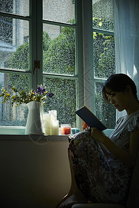 下雨天坐在窗边阅读的年轻女性夜晚时光高清图片素材