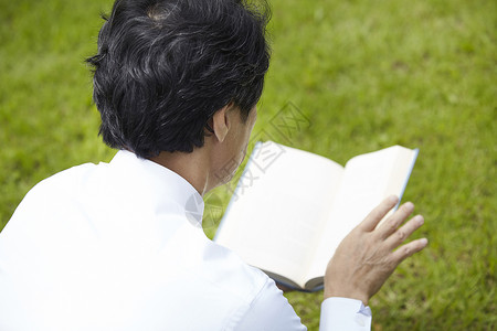 草坪上看书的成年男子背影图片