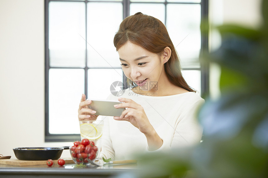 拿着手机拍摄食物的年轻女性图片