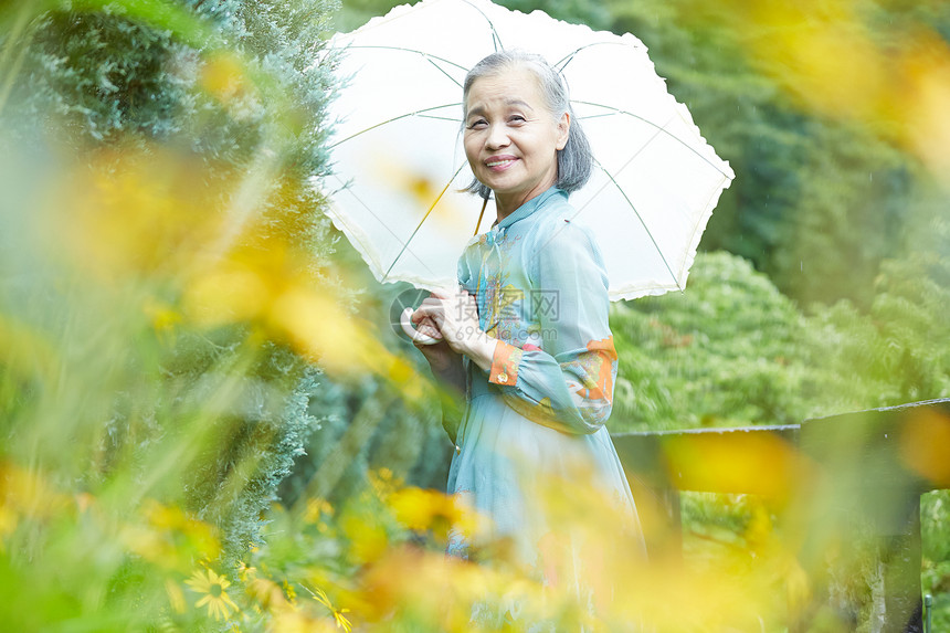 拿着遮阳伞在庭院里老妇人图片