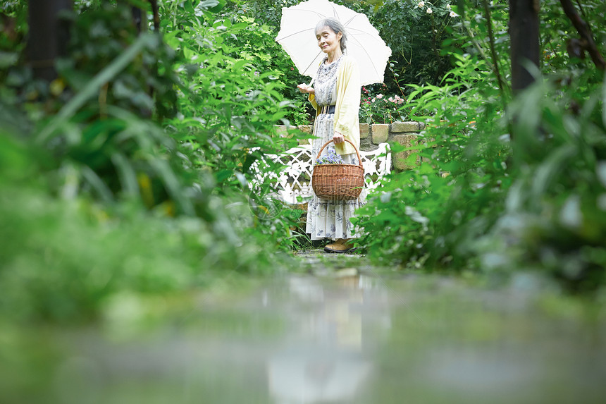 打开雨伞自然50多岁拿着遮阳伞的资深妇女在庭院里图片