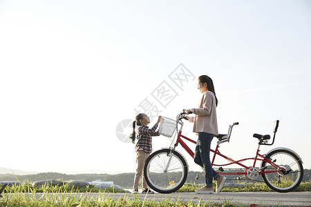 母女推行双人自行车游览公园背景图片