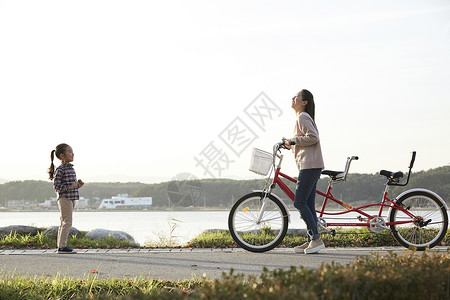 母女推行双人自行车游览公园背景图片