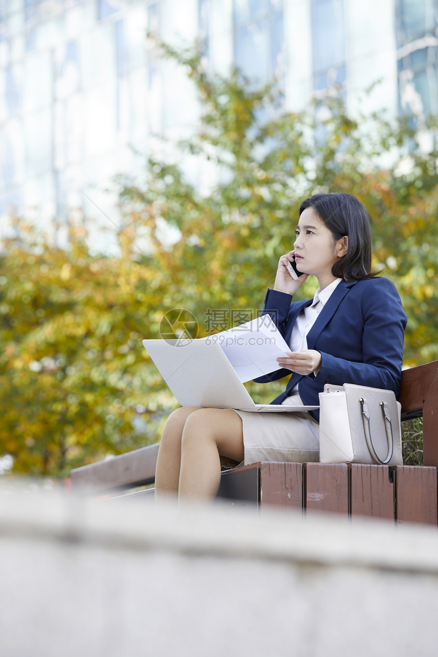 坐在长凳上打电话处理工作的女性图片