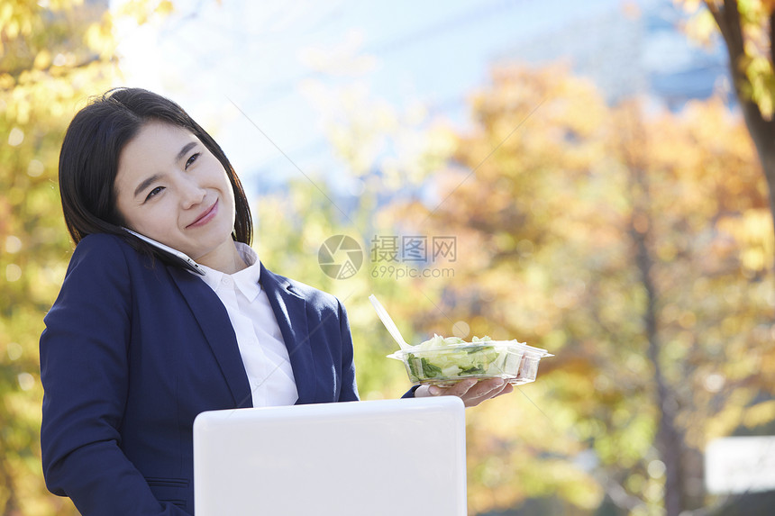 拿着沙拉歪头夹住手机打电话的女青年图片