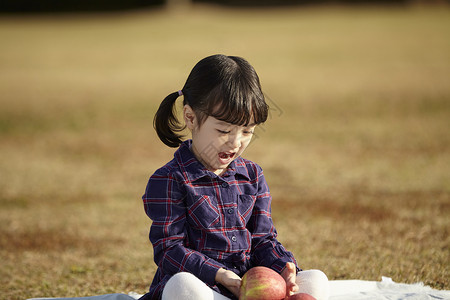 小女孩抱苹果坐在野餐垫上的小女孩抱着苹果背景