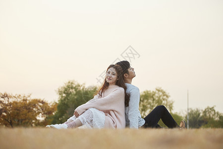 背靠背坐在草坪上的情侣图片