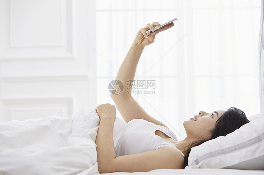 躺在床上玩手机的年轻女子图片