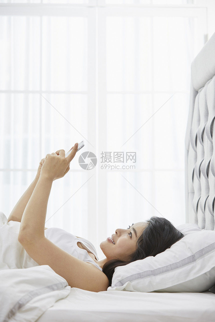 躺在床上看手机的青年女性图片