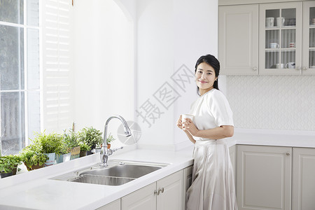 厨房里拿着水杯微笑的年轻女子杯子高清图片素材