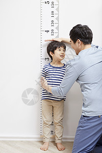 看着墙上刻度测量儿子身高的父亲图片