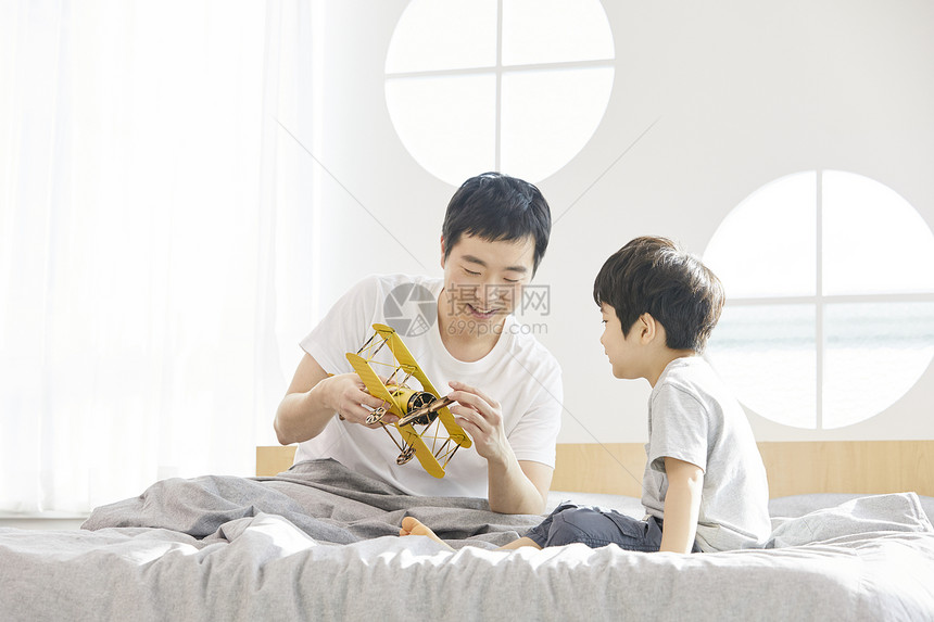 卧室里父亲拿着飞机玩具陪儿子玩耍图片