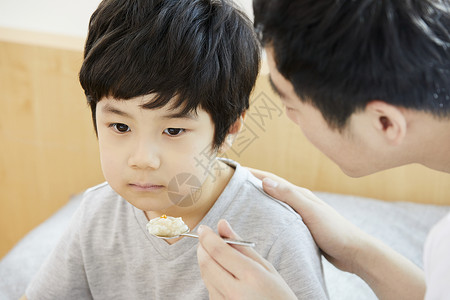 父亲拿着勺子喂食小男孩图片