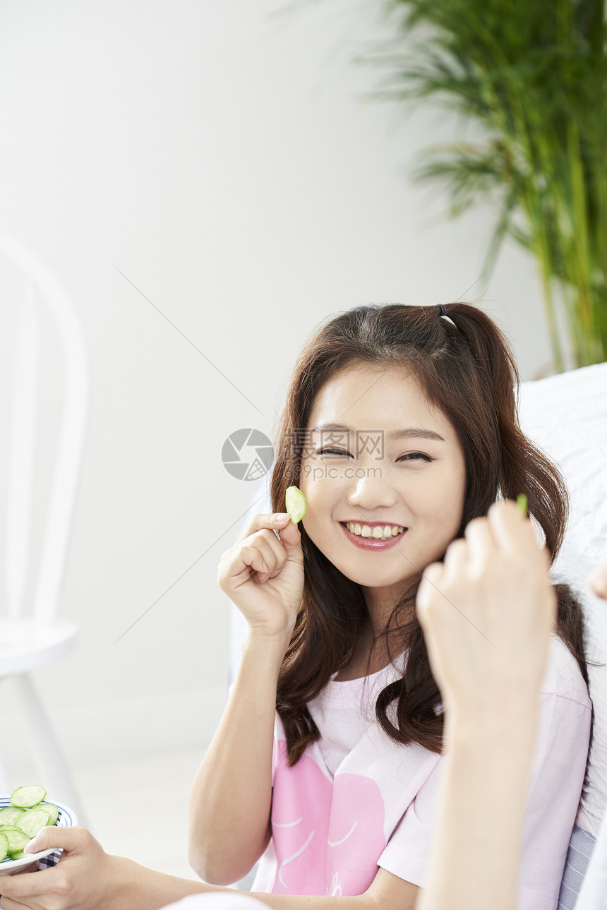 快乐的室友年轻女子用黄瓜做敷脸部图片