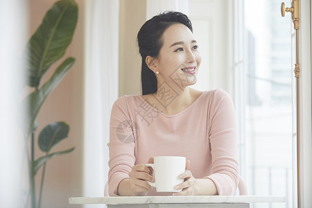 拿着咖啡看向窗外的成年女子图片