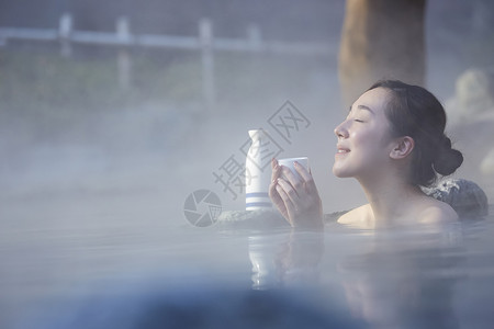 女人露天泡温泉喝清酒背景图片