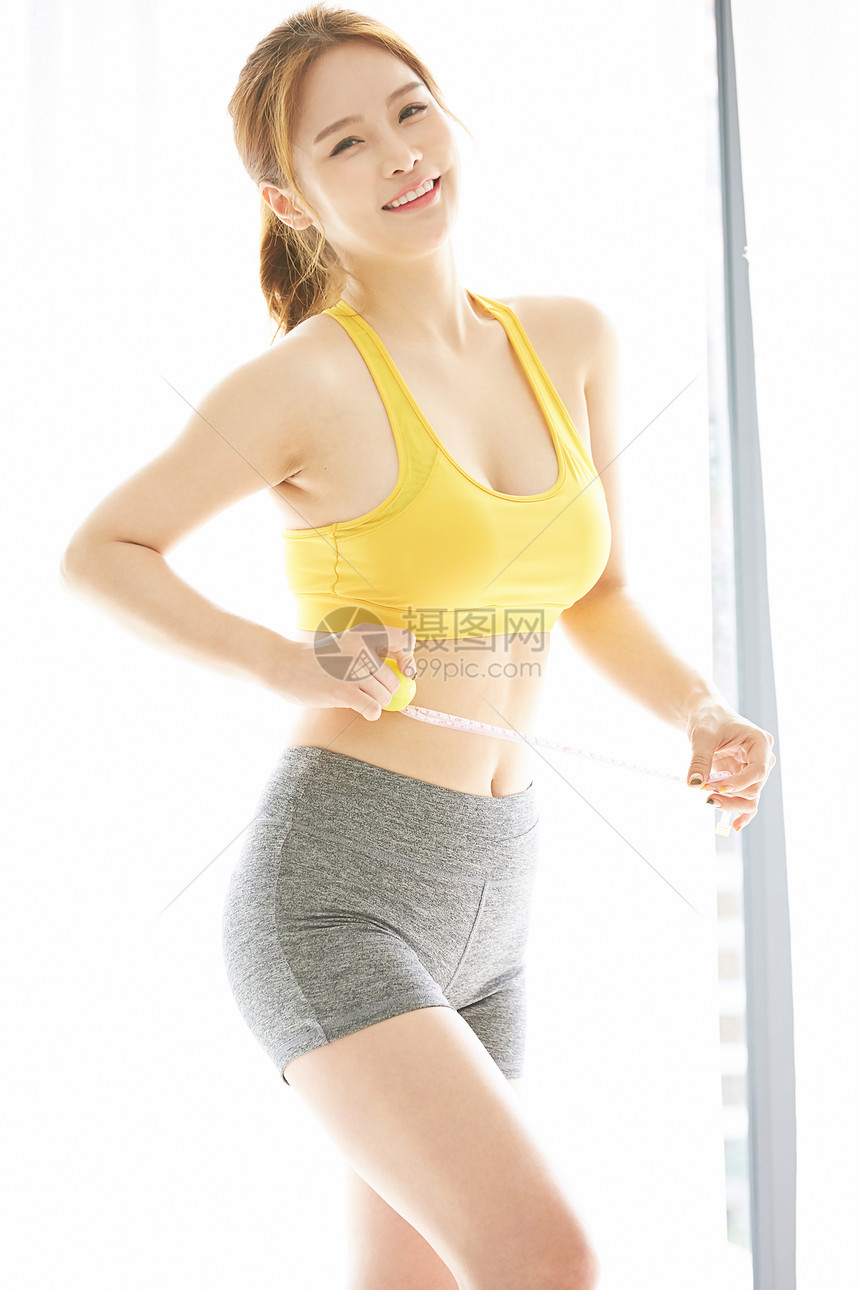 穿着运动装测量腰围的年轻女子图片