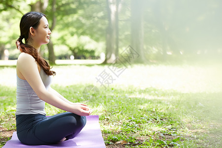 草地公园盘腿坐在瑜伽垫上的女性图片