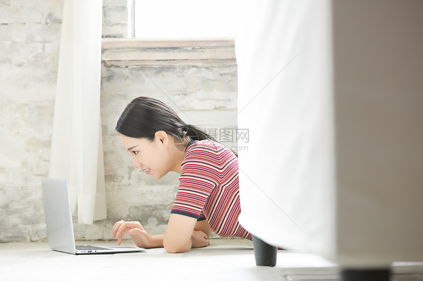 年轻女子趴在地上使用笔记本电脑图片