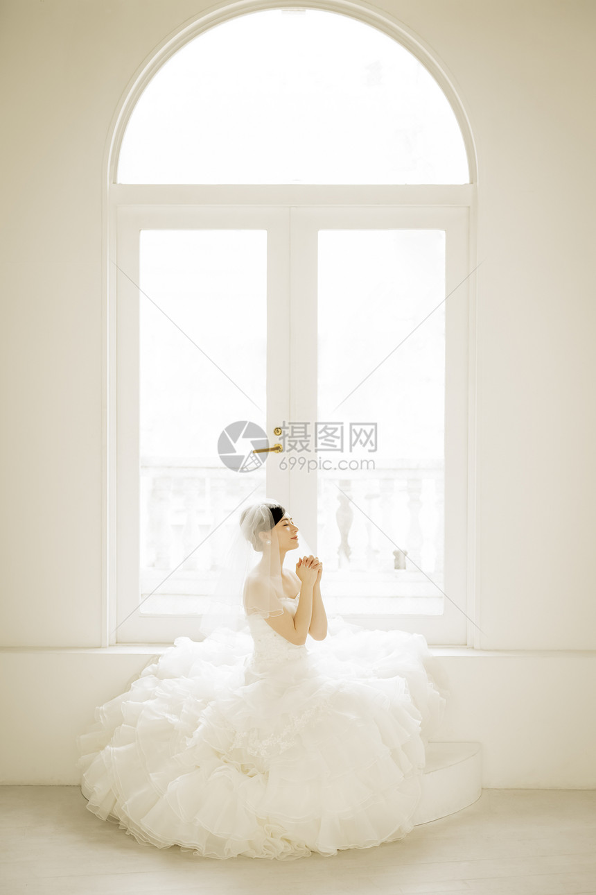 坐在窗边祈祷的婚纱美女图片