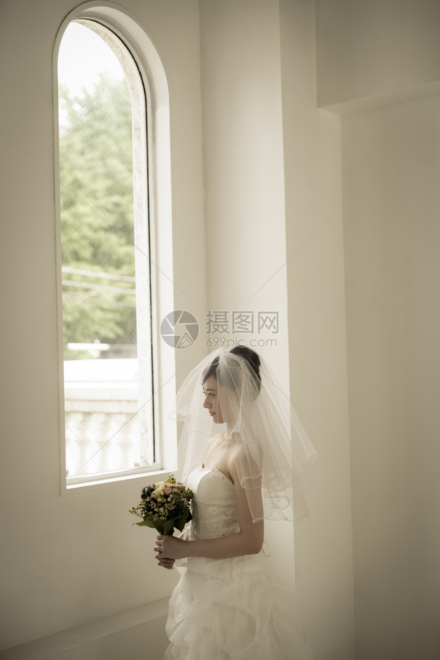 窗边戴着头纱拿着手捧花的新娘图片