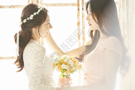 窗边拿着手捧花的美丽新娘和伴娘图片