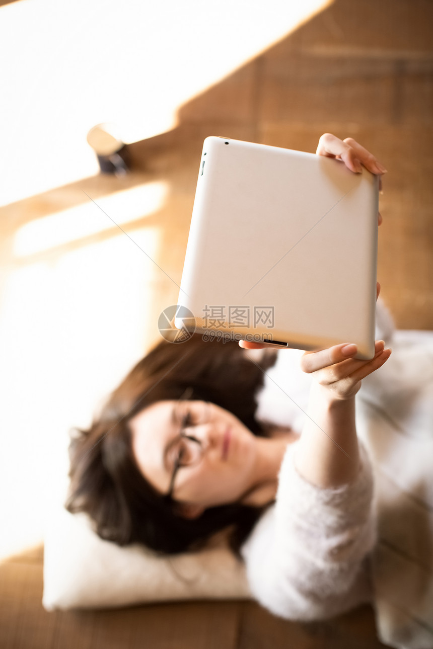 躺在地板上看平板电脑的女青年图片