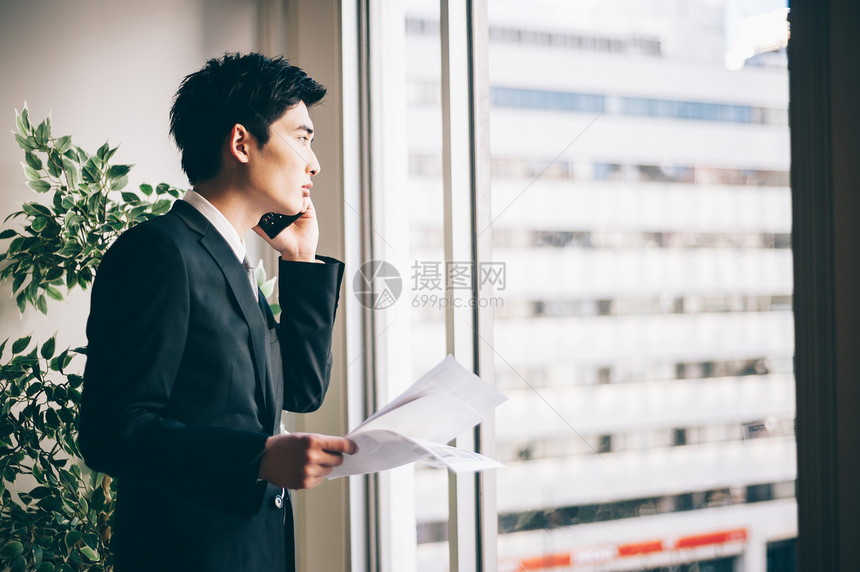 商务人士公司里30多岁新招的男在窗边打电话图片