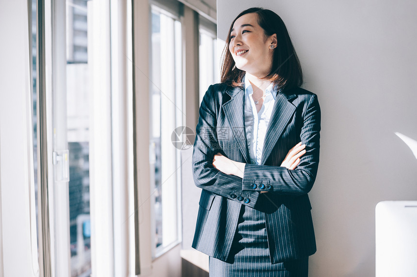 西服三十几岁商务人士倾斜在柱子的微笑的妇女在办公室图片