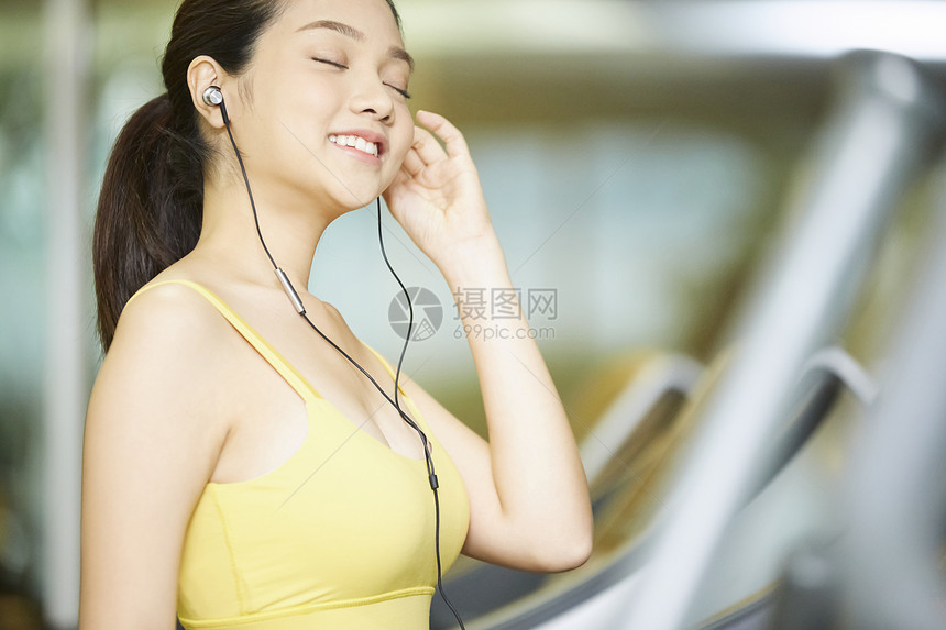 年轻女人在健身馆听音乐跑步图片