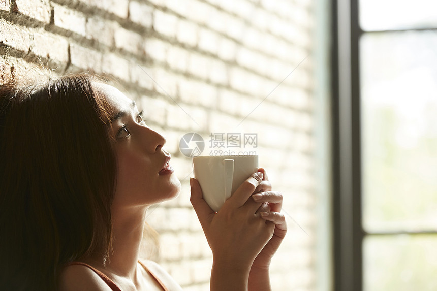 手拿咖啡杯靠在墙边的忧郁女孩图片