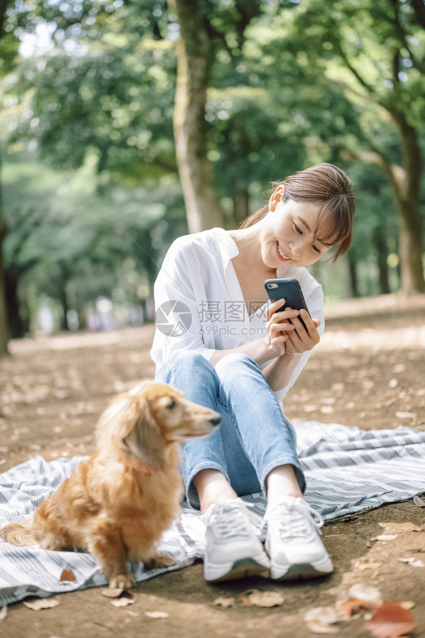 年轻女子拿着手机拍宠物狗图片