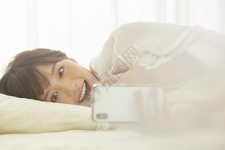 可爱女生开心的在床上看手机日光高清图片素材