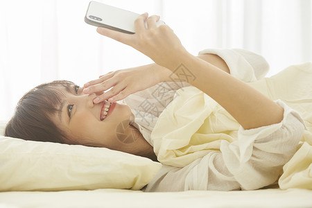 可爱女生开心的躺在床上看手机年轻女性高清图片素材