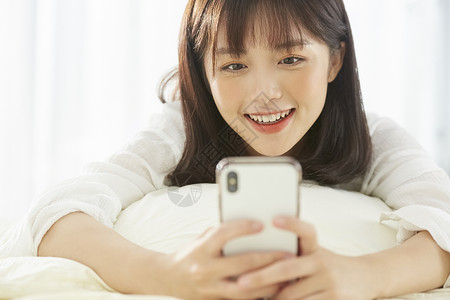 可爱女生开心的在床上看手机快乐的高清图片素材