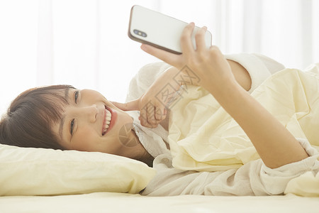 可爱女生开心的躺在床上看手机笑容高清图片素材