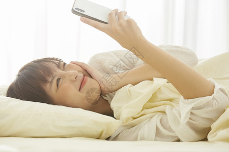 可爱女生开心的在床上看手机美人高清图片素材