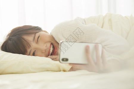 可爱女生开心的躺在床上看手机美人高清图片素材
