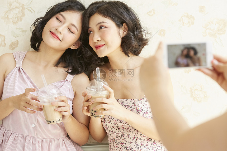 年轻姐妹淘端着奶茶拍照合影