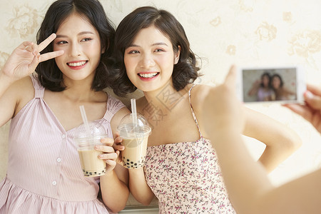 年轻姐妹淘端着奶茶拍照合影可爱高清图片素材