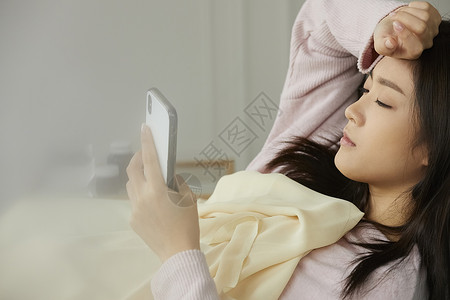 身体虚弱的女人躺在床上看手机图片