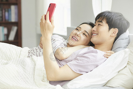 年轻夫妻紧密拥抱躺在一起看手机睡觉高清图片素材