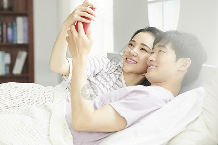 年轻夫妻紧密拥抱躺在一起看手机男女高清图片素材