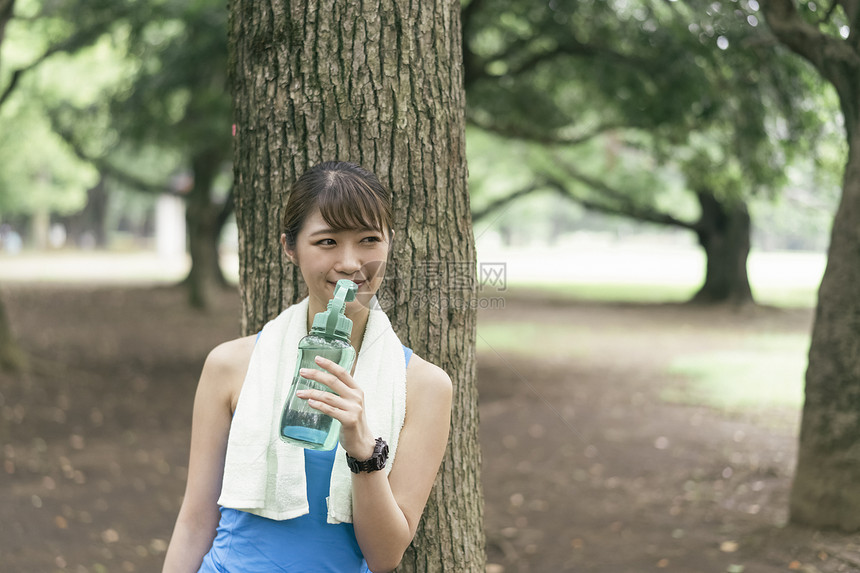 靠在树上喝水休息的青年女子图片