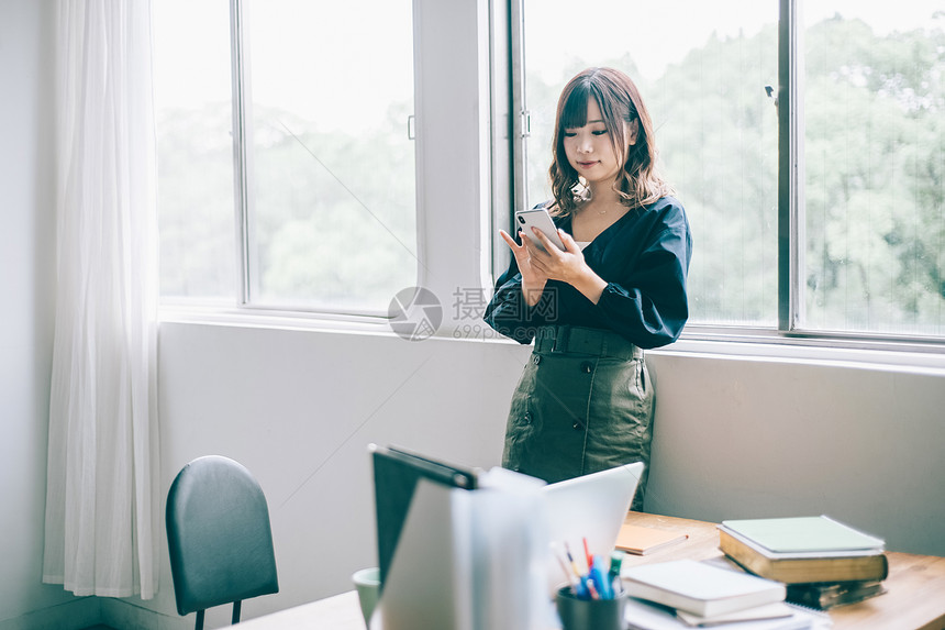 靠着窗边女人使用商务智能手机图片