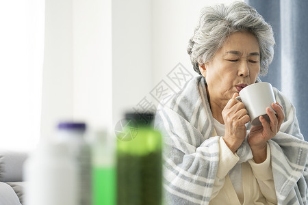 裹着毛毯生病喝水的老年女性图片